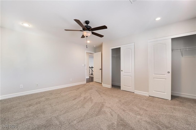 unfurnished bedroom featuring multiple closets, light carpet, and ceiling fan