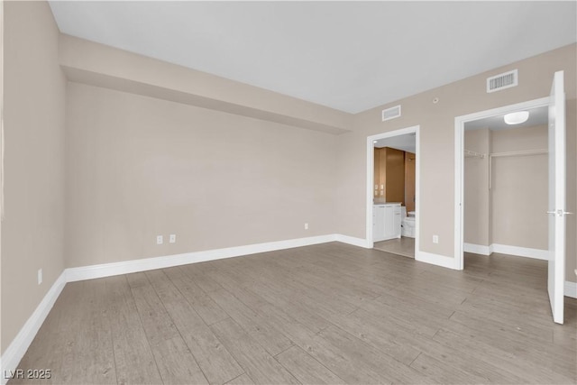 unfurnished bedroom featuring a walk in closet, wood-type flooring, a closet, and ensuite bath