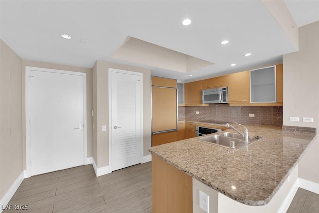 kitchen featuring sink, appliances with stainless steel finishes, tasteful backsplash, a tray ceiling, and kitchen peninsula