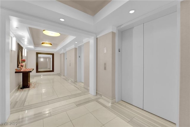 hall with a raised ceiling, elevator, and light tile patterned floors