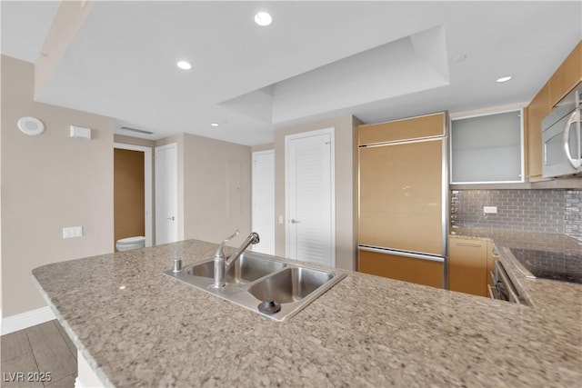 kitchen featuring sink, backsplash, paneled built in fridge, kitchen peninsula, and a raised ceiling