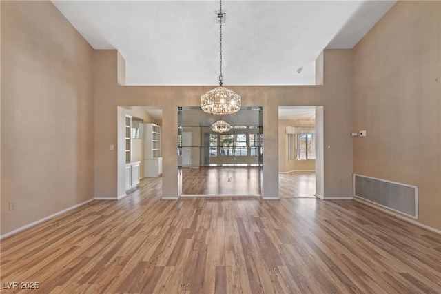 unfurnished dining area with hardwood / wood-style flooring, a high ceiling, a notable chandelier, and built in shelves