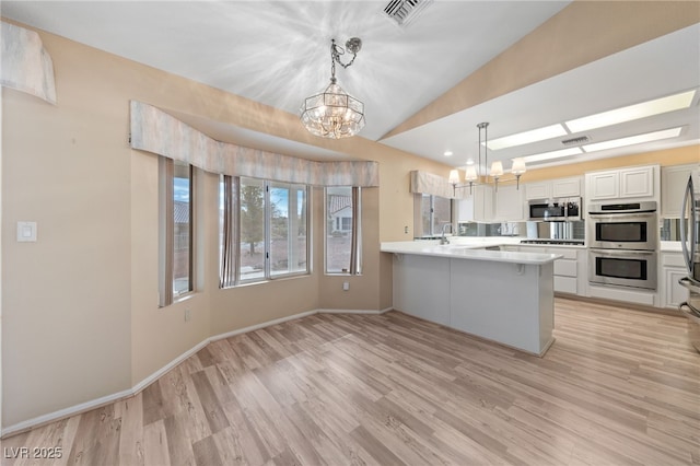 kitchen featuring an inviting chandelier, hanging light fixtures, stainless steel appliances, white cabinets, and kitchen peninsula