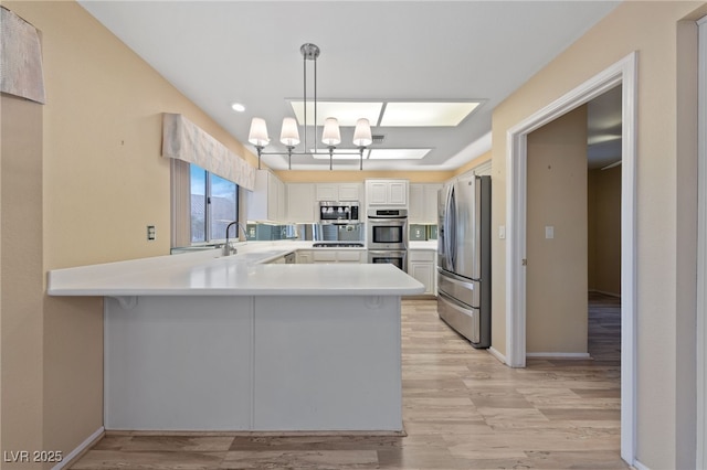 kitchen featuring appliances with stainless steel finishes, white cabinetry, sink, hanging light fixtures, and kitchen peninsula