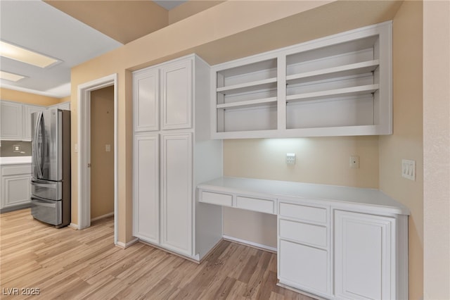 kitchen featuring white cabinetry, built in desk, stainless steel fridge, and light hardwood / wood-style flooring