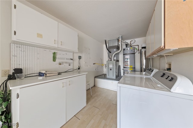 laundry area featuring secured water heater, washer and clothes dryer, cabinets, and light wood-type flooring