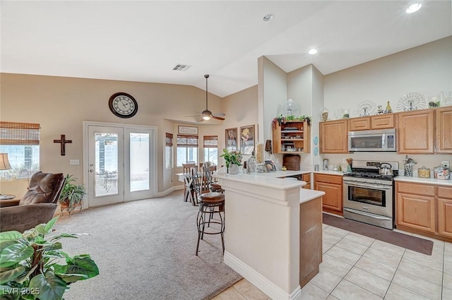 kitchen with light colored carpet, appliances with stainless steel finishes, a breakfast bar, and high vaulted ceiling