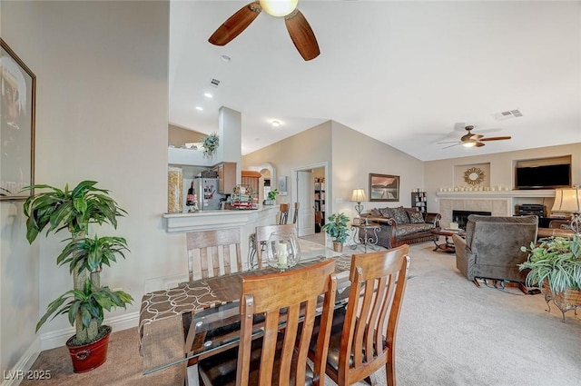 dining space featuring a fireplace, vaulted ceiling, ceiling fan, and carpet