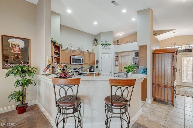 kitchen with range, a kitchen bar, vaulted ceiling, light tile patterned flooring, and kitchen peninsula