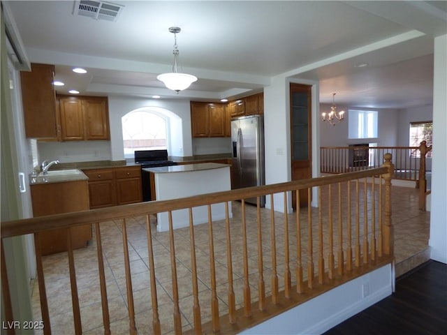 kitchen featuring black stove, sink, decorative light fixtures, a chandelier, and stainless steel fridge with ice dispenser