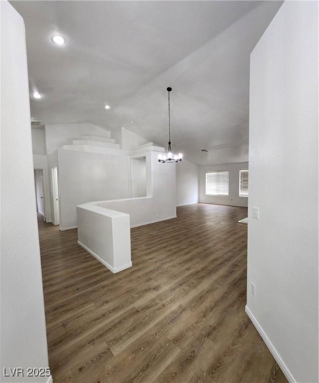 unfurnished living room featuring vaulted ceiling, dark wood-type flooring, and a notable chandelier