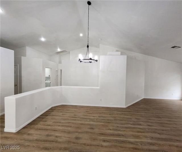 unfurnished dining area featuring a notable chandelier, washer / dryer, dark wood-type flooring, and vaulted ceiling