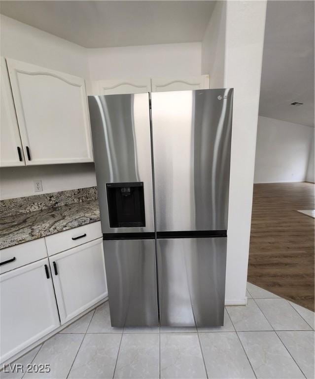 kitchen with white cabinetry, stainless steel fridge, light tile patterned flooring, and dark stone countertops