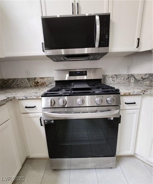 kitchen featuring stainless steel appliances, light tile patterned floors, white cabinets, and light stone counters