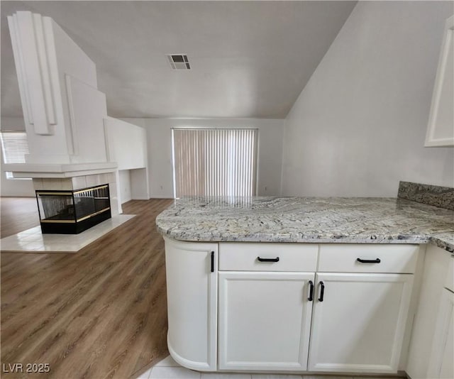 kitchen with wood-type flooring, a fireplace, light stone countertops, and white cabinets