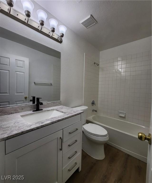 full bathroom with tiled shower / bath, hardwood / wood-style floors, vanity, toilet, and a textured ceiling