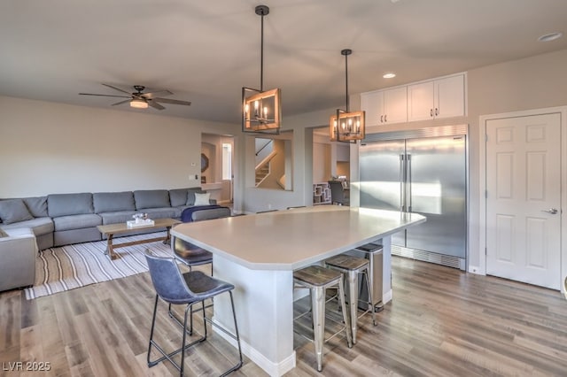 kitchen featuring a breakfast bar, white cabinets, built in fridge, pendant lighting, and light wood-type flooring