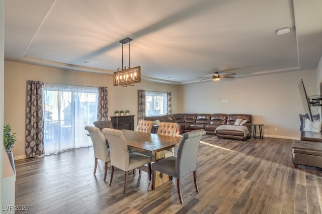 dining area featuring a tray ceiling, baseboards, and dark wood finished floors