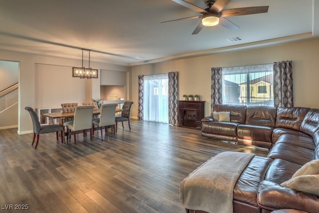 living area with visible vents, dark wood-type flooring, a healthy amount of sunlight, and ceiling fan with notable chandelier