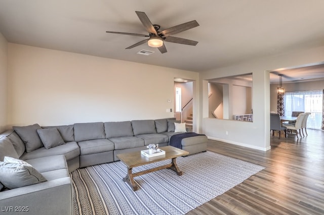 living room featuring stairway, baseboards, visible vents, dark wood finished floors, and ceiling fan