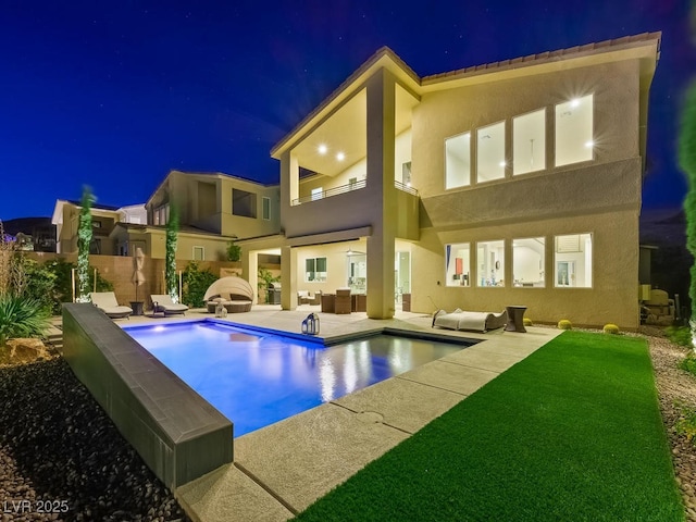 back house at night with a balcony, outdoor lounge area, and a patio