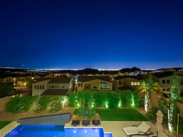 pool at night featuring a patio area and a lawn