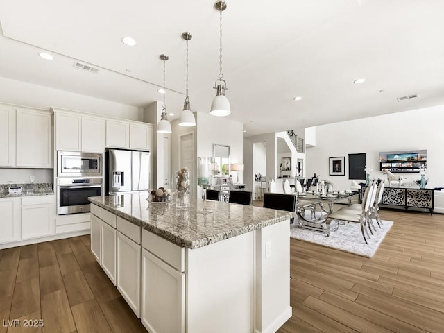 kitchen with a center island, hanging light fixtures, stainless steel appliances, light stone countertops, and white cabinets