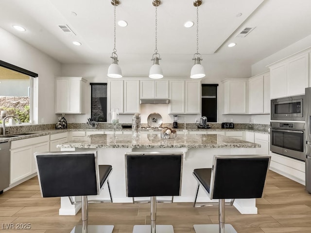 kitchen with sink, hanging light fixtures, stainless steel appliances, white cabinets, and a kitchen island