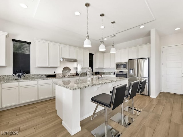 kitchen featuring stainless steel appliances, light stone counters, white cabinets, a center island with sink, and decorative light fixtures