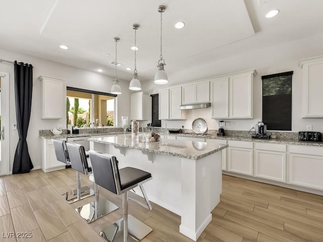 kitchen with a kitchen island, white cabinetry, a breakfast bar area, hanging light fixtures, and light stone counters