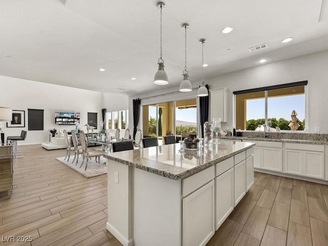 kitchen with a kitchen island, white cabinetry, sink, hanging light fixtures, and light stone counters