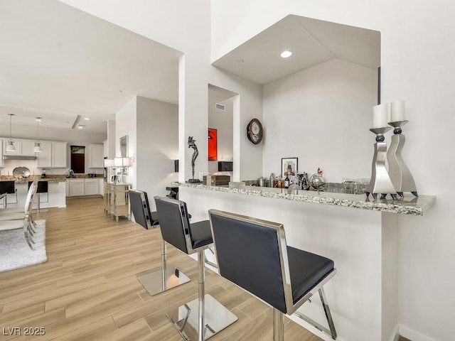 kitchen with a breakfast bar, white cabinets, kitchen peninsula, light stone countertops, and light wood-type flooring