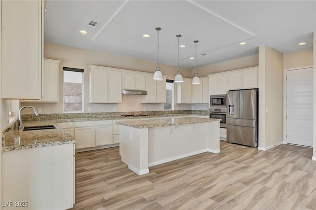 kitchen with sink, a center island, pendant lighting, stainless steel appliances, and light stone countertops