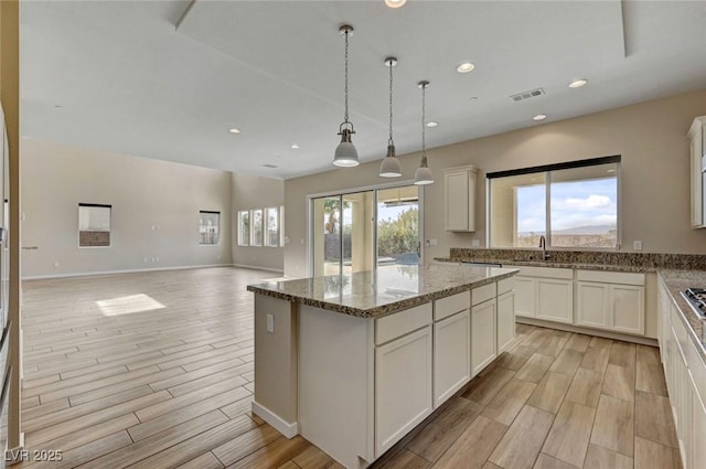 kitchen with stone countertops, decorative light fixtures, white cabinets, a center island, and stainless steel gas cooktop