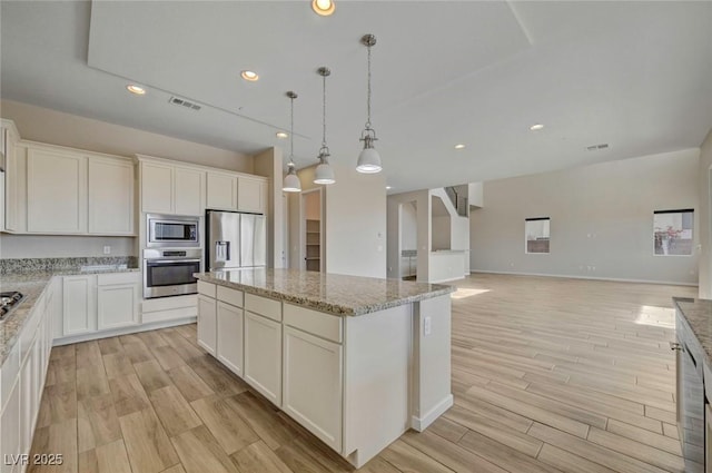 kitchen featuring light stone counters, decorative light fixtures, a center island, stainless steel appliances, and white cabinets