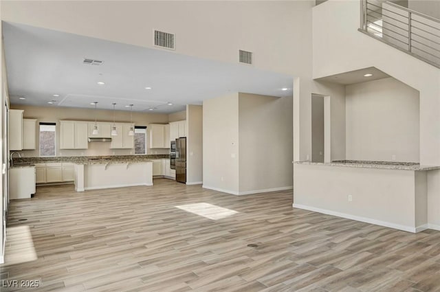 unfurnished living room with sink, a high ceiling, and light wood-type flooring