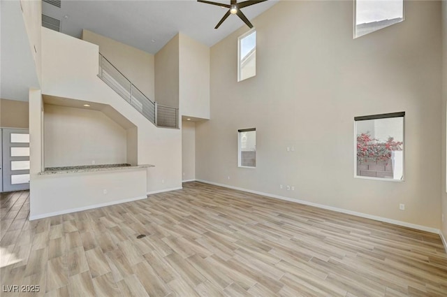 unfurnished living room with a high ceiling, ceiling fan, and light wood-type flooring