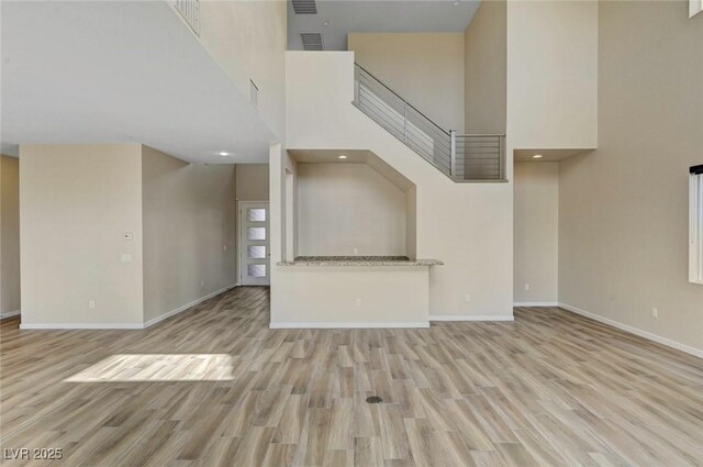 unfurnished living room featuring a high ceiling and light hardwood / wood-style floors