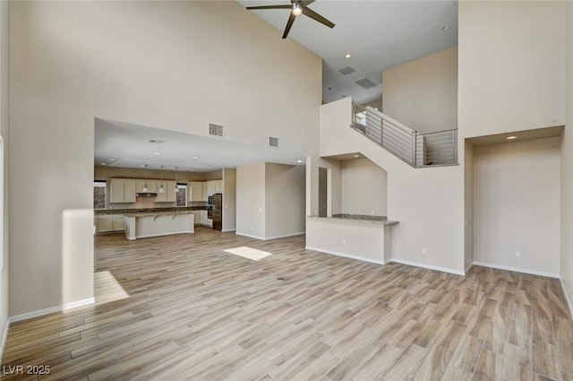 unfurnished living room with ceiling fan, a towering ceiling, and light wood-type flooring