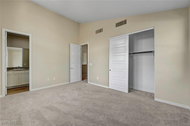 unfurnished bedroom with ensuite bathroom, lofted ceiling, sink, light colored carpet, and a closet