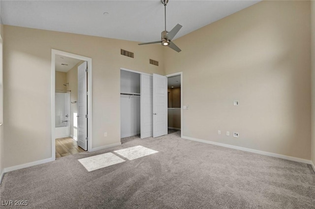 unfurnished bedroom featuring ceiling fan, high vaulted ceiling, ensuite bathroom, light colored carpet, and a closet