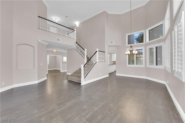 unfurnished living room featuring dark wood-type flooring, crown molding, a chandelier, and a high ceiling