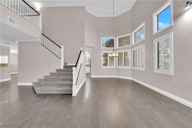 interior space featuring hardwood / wood-style flooring, crown molding, a towering ceiling, and a notable chandelier