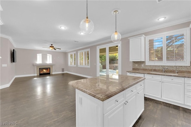 kitchen with sink, light stone counters, decorative light fixtures, a kitchen island, and white cabinets