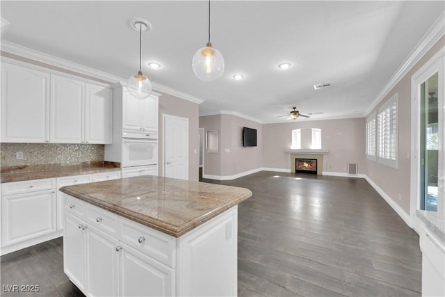 kitchen featuring hanging light fixtures, light stone countertops, a kitchen island, oven, and white cabinets