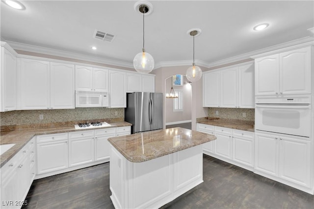 kitchen with white appliances, hanging light fixtures, light stone counters, white cabinets, and a kitchen island