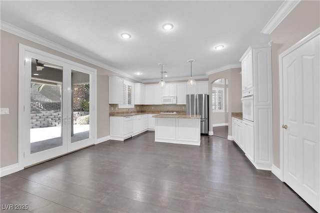 kitchen with white cabinetry, decorative light fixtures, a center island, plenty of natural light, and white appliances