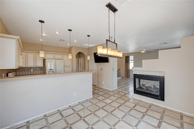 kitchen featuring fridge with ice dispenser, hanging light fixtures, decorative backsplash, and a multi sided fireplace