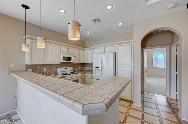 kitchen featuring decorative backsplash, hanging light fixtures, tile counters, kitchen peninsula, and white appliances