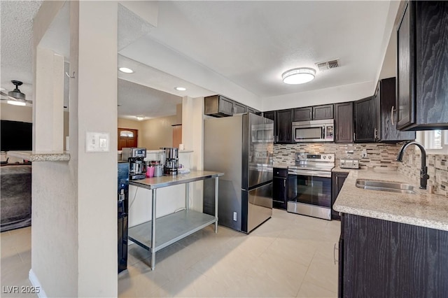 kitchen with sink, a textured ceiling, dark brown cabinets, stainless steel appliances, and backsplash